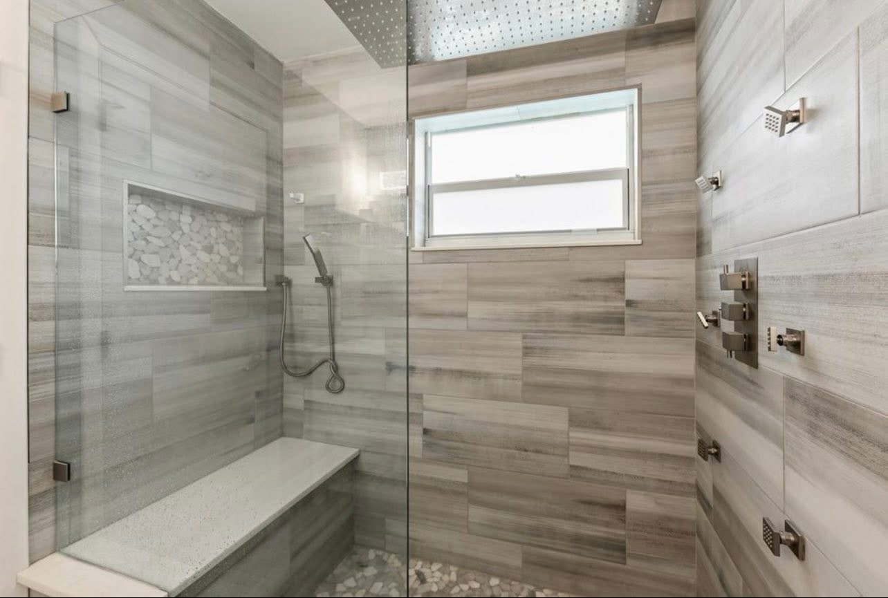 Walk-in wood-look tile shower with bench and pebble floor