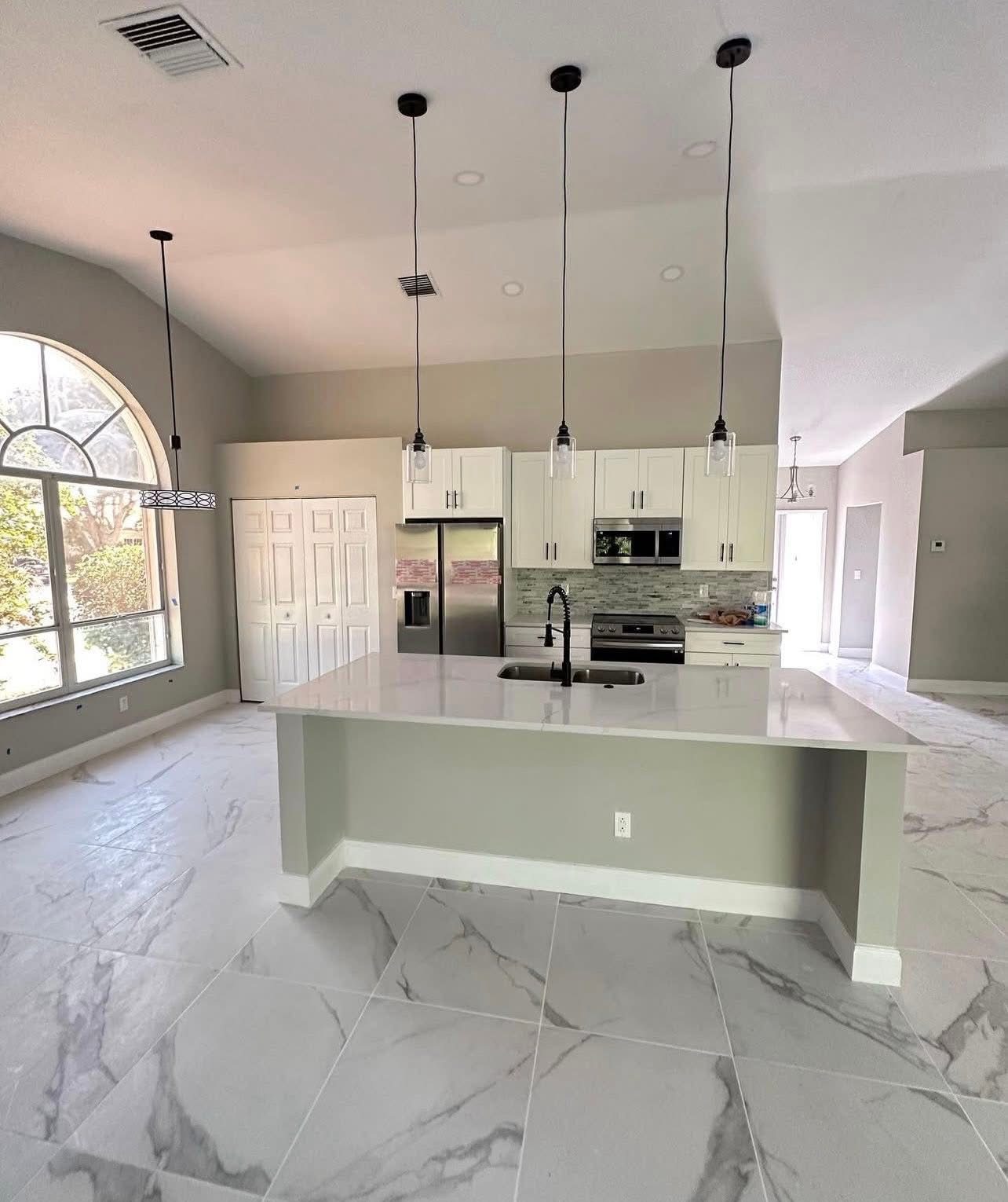 Open-concept kitchen remodel with marble floors and arched window